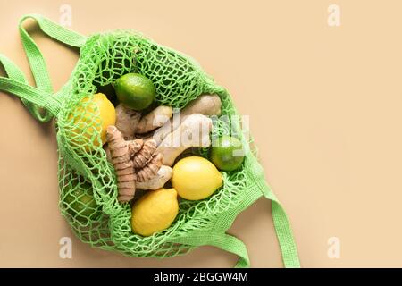 Sacco a rete verde con verdure, limone zenzero, altri alimenti su beige naturale. Zero sprechi. Cibi vegani sani. Stile di vita sostenibile. Vista dall'alto. Foto Stock