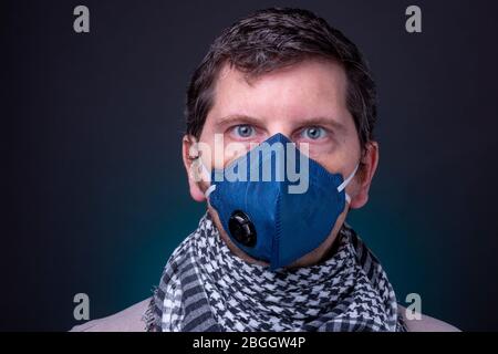 Maschera facciale blu scuro respiratore su maschio caucasico con sciarpa a scacchi. Studio basso profilo chiave di uomo con ampi occhi aperti e un look sconcertato Foto Stock