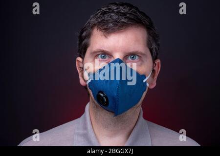 Maschera facciale per respiratore N95 blu scuro. Studio basso profilo chiave ritratto di maschio caucasico su sfondo scuro con luce rossa morbida Foto Stock