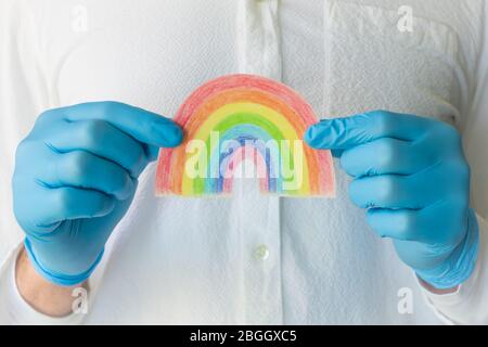 Uomo in guanto medico blu che mostra il poster dell'arcobaleno disegnato a mano. Grazie al personale NHS per il vostro servizio di fronte al concetto di crisi mondiale di coronavirus. Foto Stock