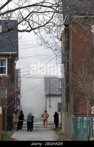 Il fumo bianco pesante che si alza dal fuoco della casa nel giorno mentre la gente guarda. Casa sul fuoco. Foto Stock