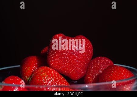 Fragole in una ciotola di vetro. Frutta aromatica. Dessert sano. Sfondo nero. Foto Stock