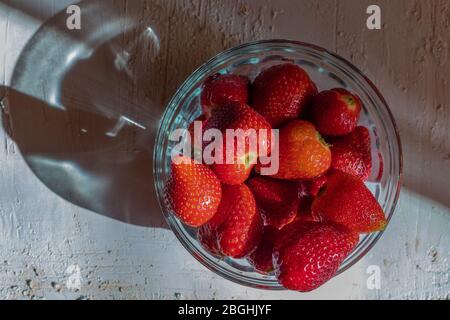 Fragole in una ciotola di vetro. Frutta aromatica. Dessert sano. Sfondo luminoso. Luce e ombra. Foto Stock