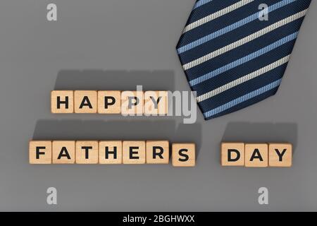 Blocchi Happy Fathers Day con cravatta su sfondo grigio. Sfondo dell'evento di celebrazione. Spazio di copia Foto Stock