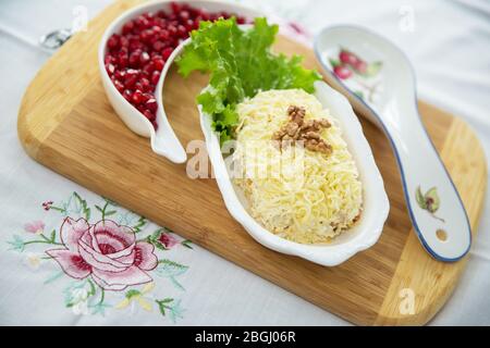 Insalata tradizionale russa Mimoza. Isolato su sfondo di legno. Vista dall'alto. INSALATA DI POLLO con noci e funghi . Melograno granulato Foto Stock