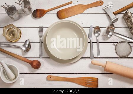 Luogo impostazione per una persona preparata su un tavolo di legno fatto di tavole bianche. Gli utensili da cucina vecchi ed eleganti sono sparsi intorno. Il tutto crea un Foto Stock