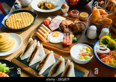 Tavolo con cibo continentale da sogno per la colazione - frutta, uova, panini, insalata, forno, bevande calde e fredde davanti alla finestra Foto Stock