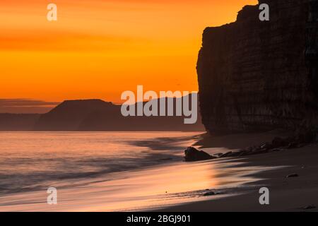 Burton Bradstock, Dorset, Regno Unito. 21 aprile 2020. Meteo Regno Unito. Ammira lungo le scogliere verso West Bay e Golden Cap mentre il cielo si illumina di un corto arancione dopo il tramonto a Hive Beach a Burton Bradstock nel Dorset, mentre il tempo regolare è in procinto di continuare questa settimana con temperature in aumento. Credito immagine: Graham Hunt/Alamy Live News Foto Stock