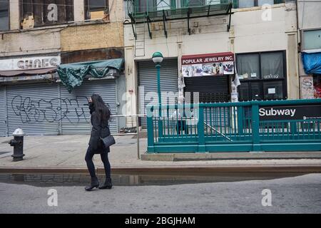 New York, New York, Stati Uniti. 17 Aprile 2020. Una donna che indossa una maschera cammina nei negozi chiusi in Canal Street a Manhattan. La maggior parte dei negozi di New York sono saliti a bordo e chiusi per affari, con certezza di quando riapriranno. Con l'aumento del numero di vittime dello stato di New York a causa dell'epidemia di coronavirus, i newyorkesi continuarono a combattere contro il COVID-19 attraverso l'isolamento sociale e l'autoquarantena, rendendo le strade e le aree pubbliche tipicamente trafficate della città silenziose. Credit: Jodi Jones/ZUMA Wire/Alamy Live News Foto Stock