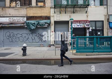 New York, New York, Stati Uniti. 17 Aprile 2020. Una donna che indossa una maschera cammina nei negozi chiusi in Canal Street a Manhattan. La maggior parte dei negozi di New York sono saliti a bordo e chiusi per affari, con certezza di quando riapriranno. Con l'aumento del numero di vittime dello stato di New York a causa dell'epidemia di coronavirus, i newyorkesi continuarono a combattere contro il COVID-19 attraverso l'isolamento sociale e l'autoquarantena, rendendo le strade e le aree pubbliche tipicamente trafficate della città silenziose. Credit: Jodi Jones/ZUMA Wire/Alamy Live News Foto Stock