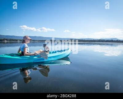 Giovane donna e cane kayak sul lago tranquillo e soleggiato, i migliori amici, isolamento calma e concetto di pace Foto Stock