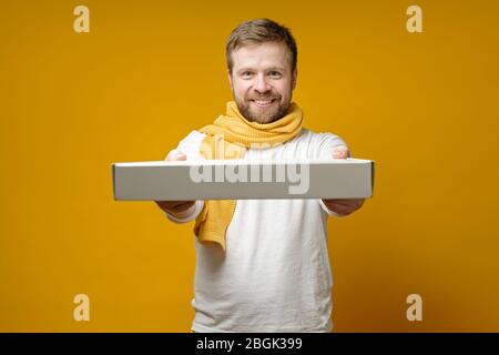 Un uomo contento che indossava una sciarpa venne a un incontro con gli amici con una pizza, lui sorridendo felicemente e tenendo fuori una scatola. Foto Stock