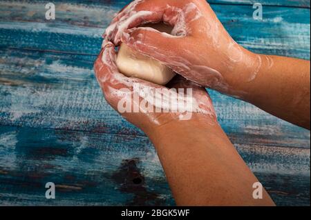 Qualcuno sta insaponando le loro mani con un pezzo di sapone da toletta su uno sfondo di legno. Primo piano. Il lavaggio delle mani con sapone è una prevenzione di COVID-19 infec Foto Stock