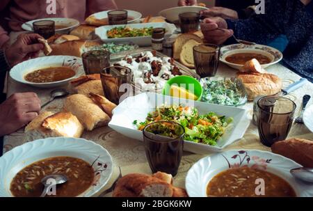 Affollata famiglia musulmana che ha iftar in un giorno ramadan con un tavolo pieno di deliziosi piatti vegani cercando Foto Stock