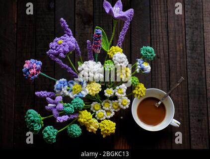 Incredibile tavolino con fiori fatti a mano e tazza di caffè su sfondo di legno, lavanda e daisy crochet per arredamento interno casa, creatività artistica Foto Stock