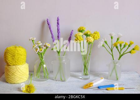 Bel prodotto fatto a mano per la decorazione domestica, dente di leone giallo, lavanda viola, fiore daisy in vaso di vetro su sfondo bianco, arte crochet Foto Stock