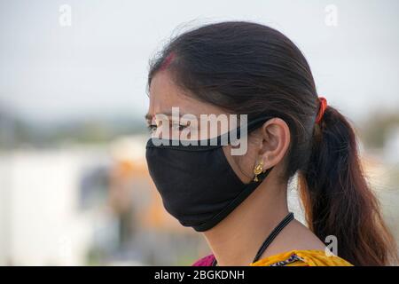 Dettaglio di donna indiana che indossa una maschera nera viso.vista laterale viso, sfondo sfocato. Virus Corona, quarantena COVID-19. Maschera come protezione. Foto Stock