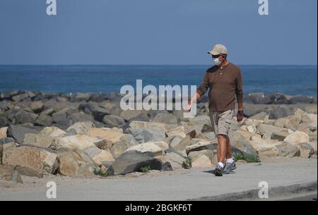 Un uomo cammina lungo la spiaggia indossando una maschera protettiva per il viso per Covid-19 Foto Stock