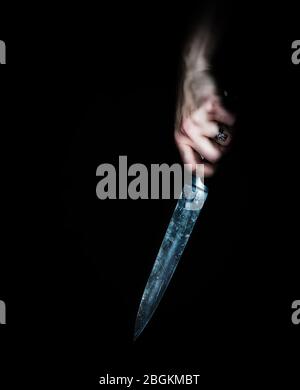 Donna che tiene un coltello grande in mano contro un fondo nero, concetto di omicidio, crimine, violenza, mistero, colore Foto Stock