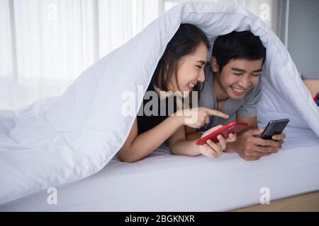 Gli amanti delle coppie asiatiche che si trovano sul loro telefono cellulare gioco a letto a casa Foto Stock