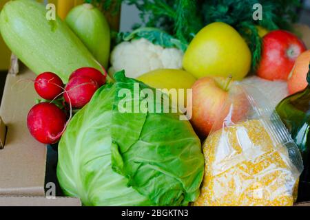 Scatola con frutta e verdura mele cavolo rafano olio zucchine, grits primo piano. Servizi di consegna di cibo durante la pandemia di coronavirus e sociale Foto Stock