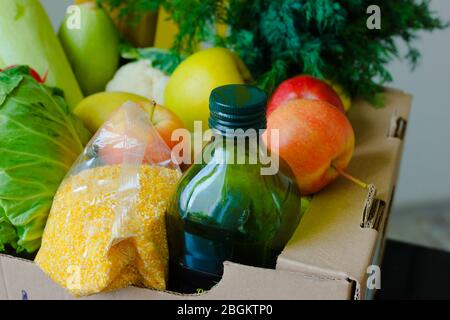 Scatola con frutta e verdura mele cavolo rafano olio zucchine, grits primo piano. Servizi di consegna di cibo durante la pandemia di coronavirus e sociale Foto Stock