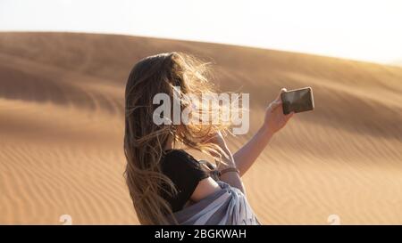 Una giovane donna fotografa un tramonto nel deserto sul suo smartphone. Foto Stock