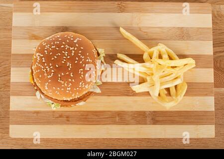 Gustoso cheeseburger con verdure e salsa in un panino di sesamo e patatine fritte su tavolo di legno Foto Stock