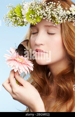 ritratto di bella ragazza giovane rossa sana in garland con farfalla su gerbera fiore su blu Foto Stock