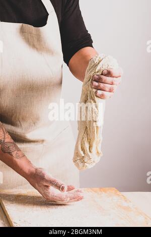 Processo concettuale di produzione di pane fatto in casa senza lievito alternativo. Un uomo impasta una pentola per impastare con l'impasto sul tavolo. Foto Stock