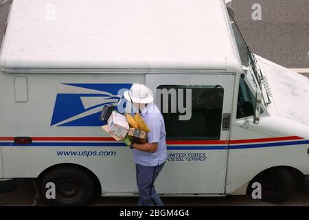 Los Angeles, CA / USA - 20 aprile 2020: Un corriere postale per il servizio postale degli Stati Uniti USPS indossa una maschera e guanti durante la pandemia COVID-19. Foto Stock