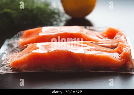 Filetti di pesce rosso o salmone in confezione sottovuoto su fondo nero. Concetto di alimentazione sana. Omega-3. Messa a fuoco selettiva. Foto Stock