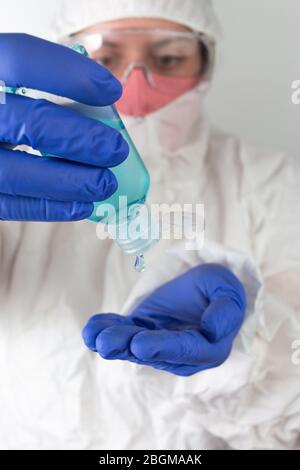 Medico in indumenti protettivi indossare su gel igienizzante blu alcol, disinfettante per le mani. Prevenzione pandemica, coronavirus Foto Stock