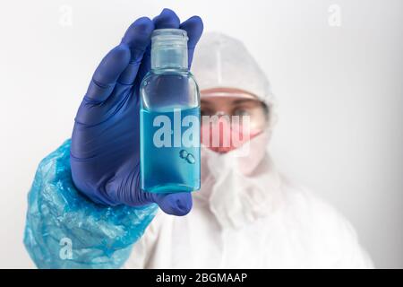 Medico in indumenti protettivi che contiene una bottiglia di gel igienizzante blu alcol, disinfettante per le mani, protezione da coronavirus, pandemia Foto Stock