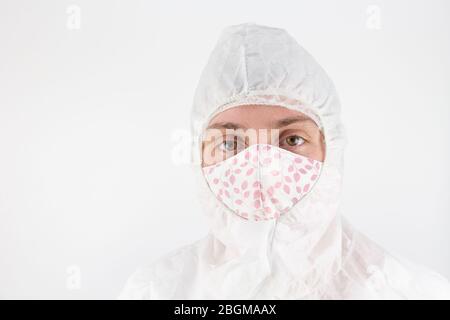 Donna in abbigliamento medico protettivo che indossa una maschera faccia in tessuto fatto in casa. Prevenzione pandemica, protezione del viso cucito Foto Stock
