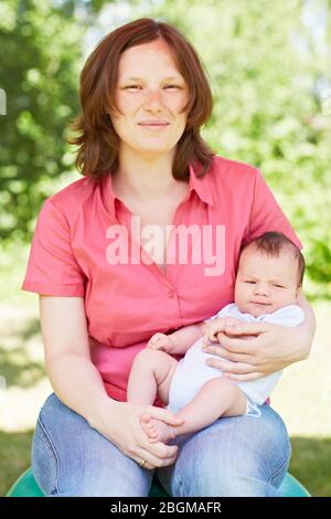 Glückliche Mutter im Grünen mit ihrem Baby auf dem Schoß Foto Stock