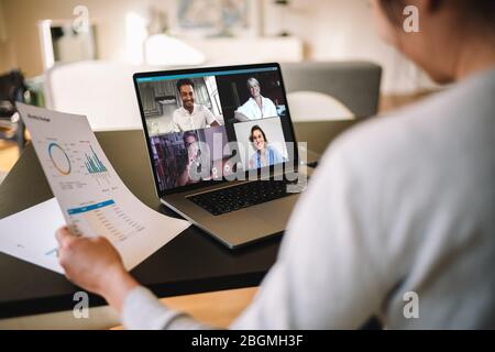 Donna che tiene un rapporto di affari che lavora a casa avendo una video conferenza con i colleghi. Vista a spalla di una donna d'affari che ha un autobus online Foto Stock