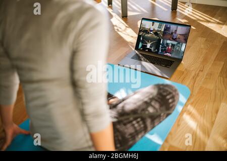 Guarda dal retro di una donna che ha una lezione di yoga virtuale con un gruppo di persone a casa durante una videoconferenza. Fitness trainer che prende lezioni di yoga online ove Foto Stock