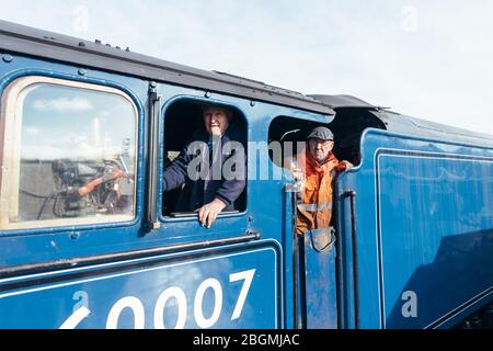 Due uomini che si affacciano dalla cabina di lavoro della locomotiva britannica a vapore, il Sir Nigel Gresley (LNER Classe A4 Pacific 4498), in British Railways (BR) blu Foto Stock