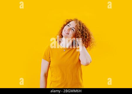 Immagine a mezza lunghezza di una donna felice sognante con capelli rossi ricci su giallo Foto Stock