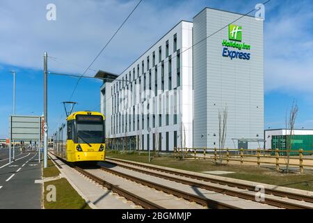 Tram Metrolink che passa dall'Holiday Inn Express il giorno di apertura della Trafford Park Line, 22 marzo 2020. Barton Dock Rd., Trafford, Manchester, Regno Unito Foto Stock