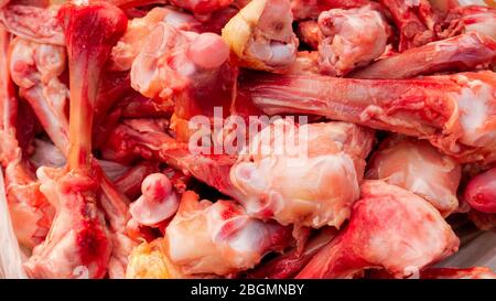 Molte ossa di pollo sguingiate crude nel mucchio giacciono sul tavolo. Mangiare persone povere o mangiare per i cani. Messa a fuoco selettiva. Primo piano. Illuminazione naturale. Foto Stock