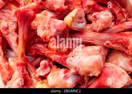 Molte ossa di pollo sguingiate crude nel mucchio giacciono sul tavolo. Mangiare persone povere o mangiare per i cani. Messa a fuoco selettiva. Primo piano. Illuminazione naturale. Foto Stock