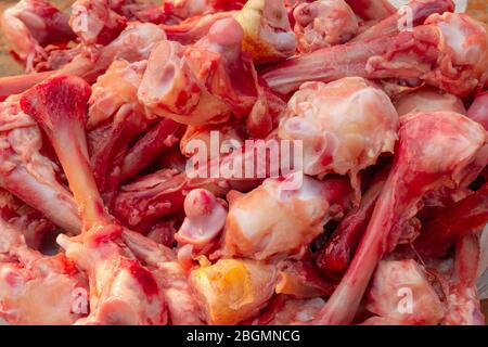 Molte ossa di pollo sguingiate crude nel mucchio giacciono sul tavolo. Mangiare persone povere o mangiare per i cani. Messa a fuoco selettiva. Primo piano. Illuminazione naturale. Foto Stock