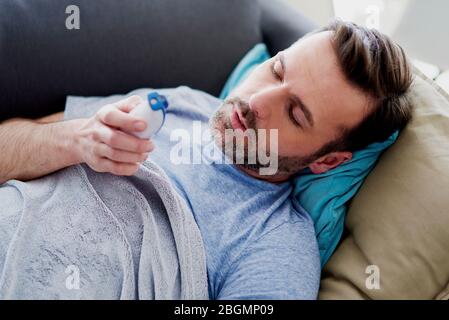 Uomo malato con temperatura elevata che rimane a letto Foto Stock