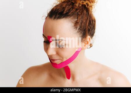 Divertente donna timida con nastro rosa antirughe sul suo viso su bianco Foto Stock