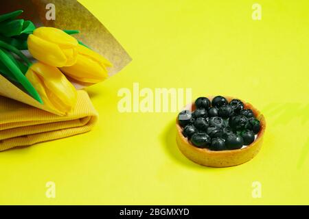Fiori e torta. Composizione monocromatica elegante e alla moda in colore giallo su sfondo studio. Vista dall'alto, disposizione piatta. Pura bellezza delle cose usuali intorno. CopySpace per l'annuncio. Vacanza, cibo, moda. Foto Stock