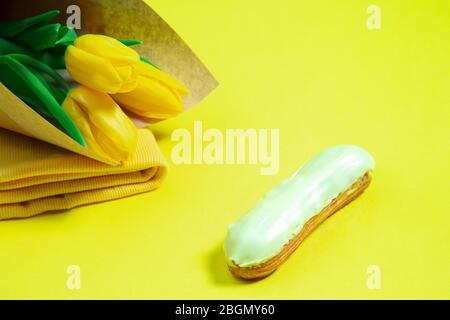 Fiori e torta. Composizione monocromatica elegante e alla moda in colore giallo su sfondo studio. Vista dall'alto, disposizione piatta. Pura bellezza delle cose usuali intorno. CopySpace per l'annuncio. Vacanza, cibo, moda. Foto Stock