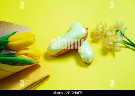 Fiori e torta. Composizione monocromatica elegante e alla moda in colore giallo su sfondo studio. Vista dall'alto, disposizione piatta. Pura bellezza delle cose usuali intorno. CopySpace per l'annuncio. Vacanza, cibo, moda. Foto Stock