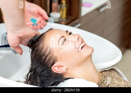 Donna che riceve lavando i capelli nel lavandino con le mani del parrucchiere che ride nel salone di parrucchiere. Foto Stock